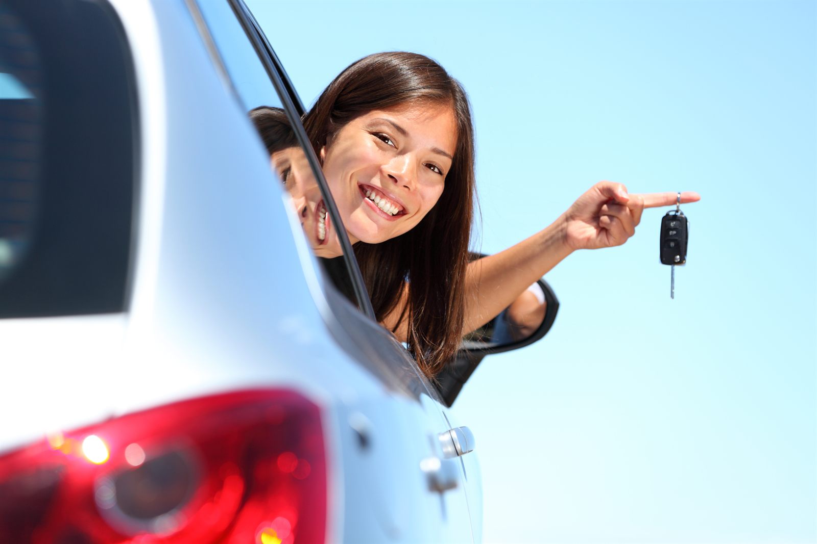 Smiling woman leaning out of a car window holding keys